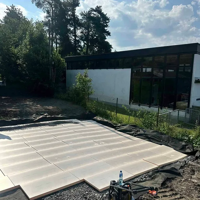 Isolasjonsplater lagt på grusgrunn ved bygg under oppføring.