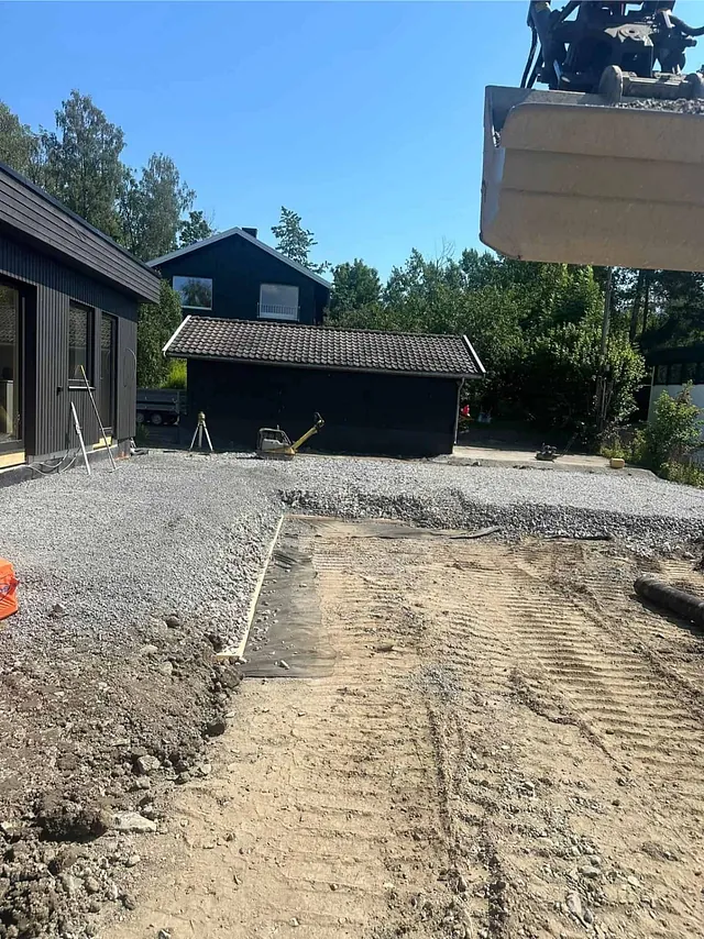 Planert tomt med grus og anleggsmaskin i arbeid ved bolig.